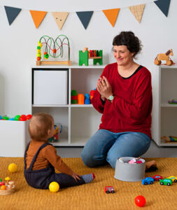 Teacher playing with a toddler beside toy shelves